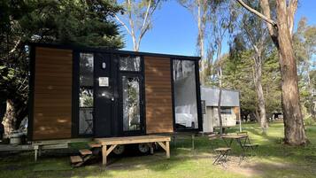 Un moderno e compatto camper con esterno nero e dettagli in legno, immerso in un'area erbosa con alberi sullo sfondo.