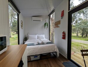 Ein Schlafzimmer mit einem Bett, einem Holztisch, einer Mikrowelle, einem Feuerlöscher und Blick ins Freie.