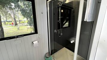 Et moderne badeværelse med en glasafskærmet brusekabine, toilet og et vindue med udsigt til en have.