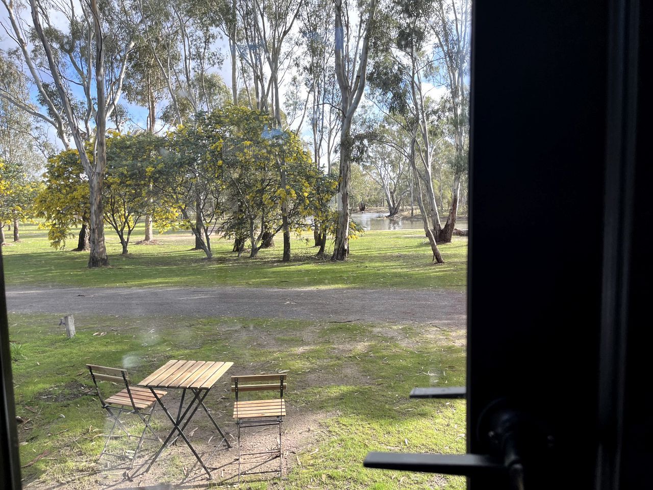 Ein Sitzbereich im Freien mit Tisch und Stühlen, umgeben von Bäumen und einer Wiese.