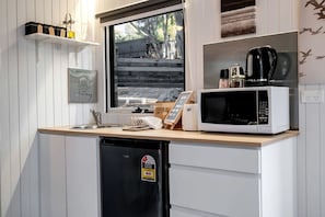A compact kitchen with a built-in microwave, a coffee maker, and a dishwasher. - Countryside Tiny House for a Pet Friendly Glamping Getaway in Howes Creek, Victoria (Mansfield)
