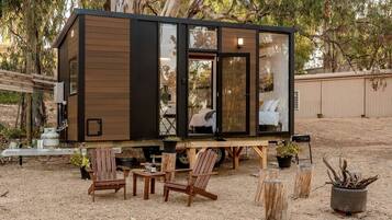 Een modern, compact vakantiehuisje met een grote schuifpui, een houten terras en een zitgedeelte buiten.