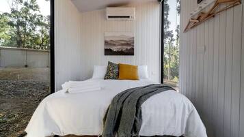 A bedroom with a bed, white bedding, a single yellow pillow, a gray throw blanket, and a picture on the wall.