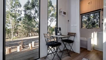 A room with a wooden table and chairs, a bench, a window, and a view of trees outside.