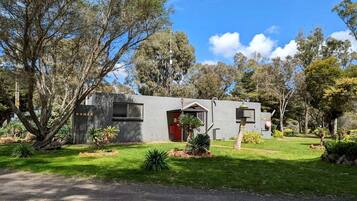 A modern two-story house with a red door, surrounded by a well-maintained garden and trees.