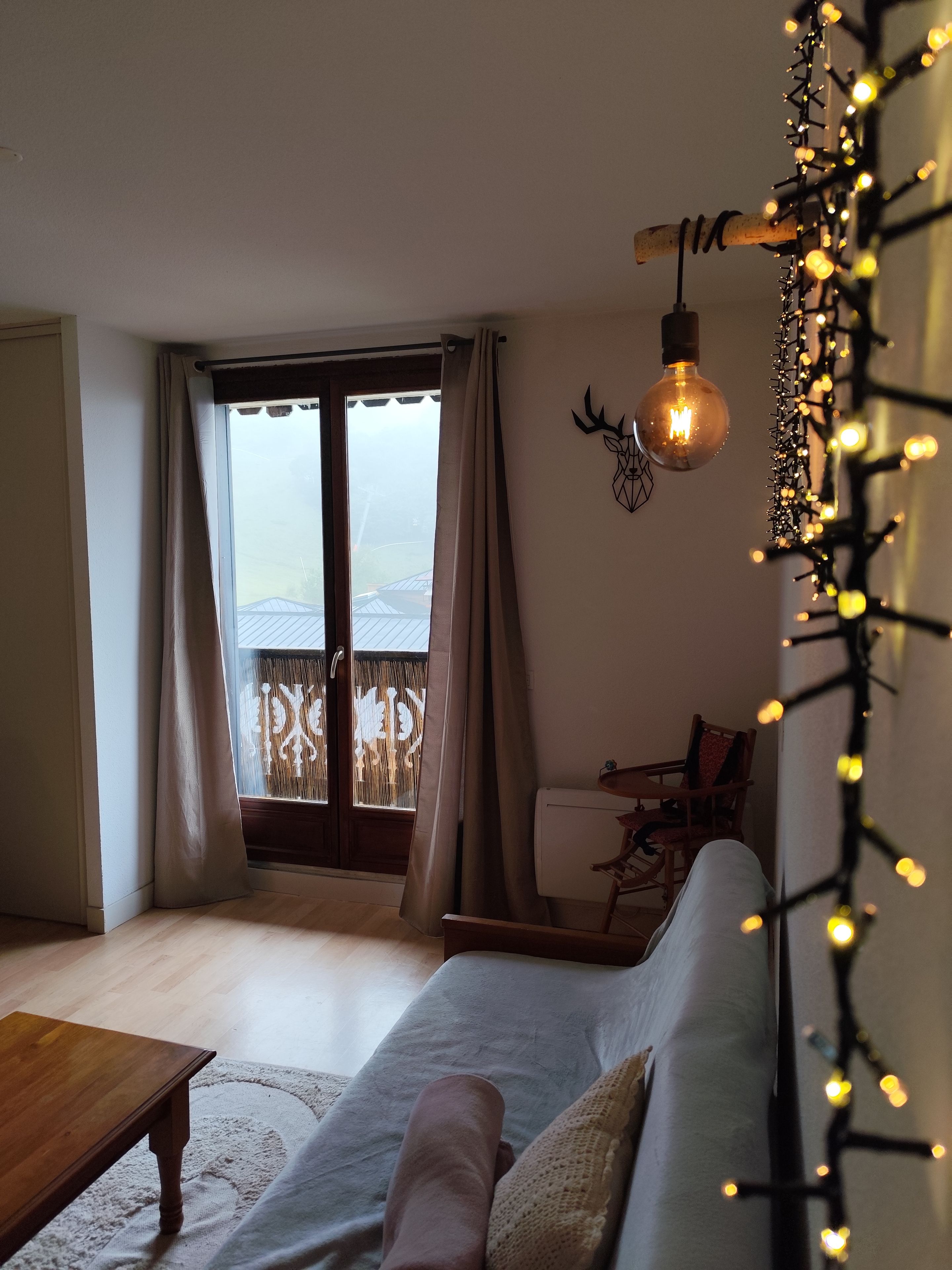 Una sala de estar con sofá, una mesa de centro de madera, una lámpara decorativa y vistas a través de un ventanal.