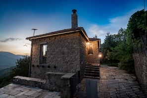 A stone building with a chimney, a small window, and a staircase leading to a door.