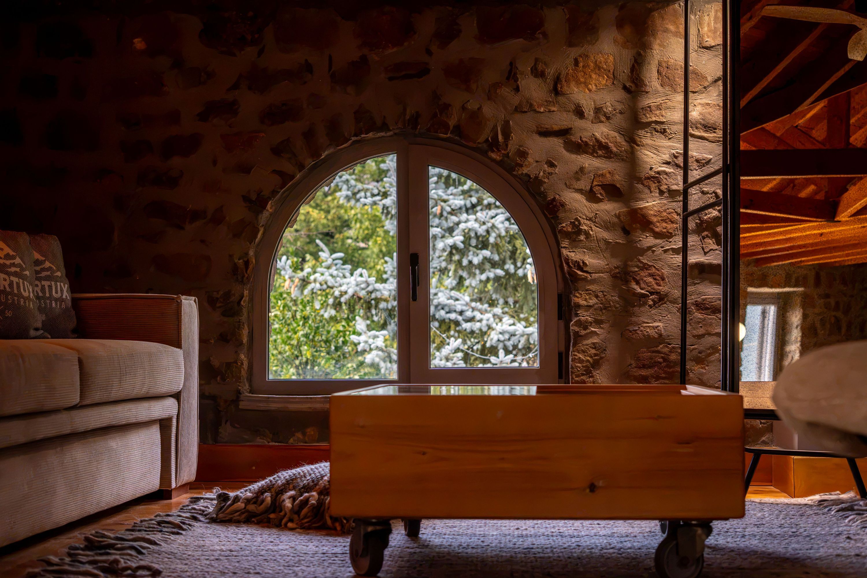 A cozy room with a stone wall, a large arched window, a wooden bench, and a sofa.