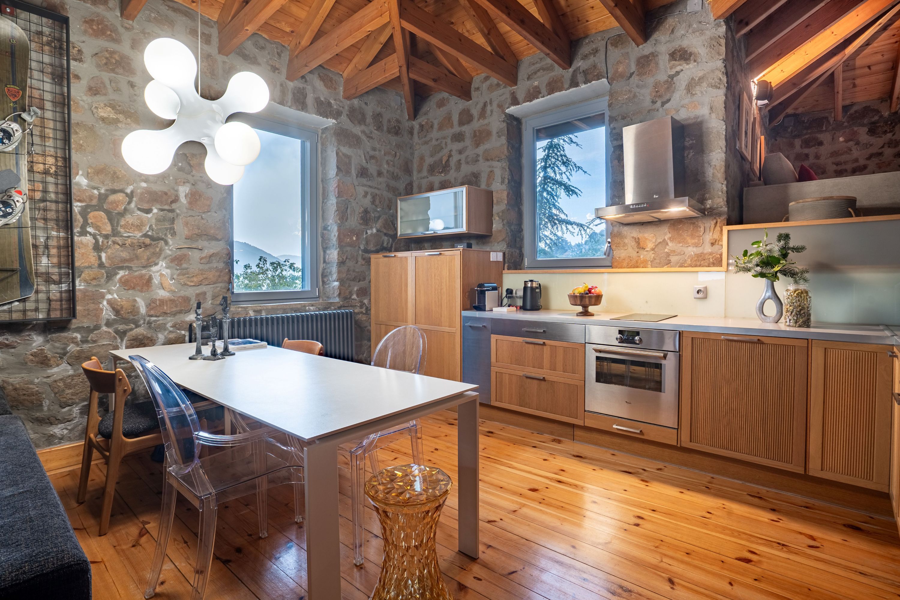 A rustic kitchen with stone walls, wooden beams, and a large window.
