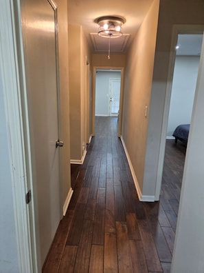 A hallway with wooden flooring, white walls, and a ceiling light fixture. - Spacious 4-bedroom apartment in a safe, quiet and matured Neighborhood (Doraville)