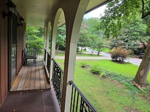 A covered porch with a wooden floor and metal railing, overlooking a well-maintained lawn and trees. - Spacious 4-bedroom apartment in a safe, quiet and matured Neighborhood (Doraville)