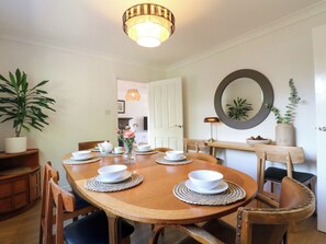 A dining area with a round wooden table, white plates, and bowls, surrounded by wooden chairs. - 7 Forge Close (Derby)