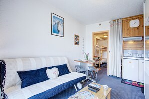 Una sala acogedora con un sofá, una mesa de comedor y una zona de cocina con refrigerador.