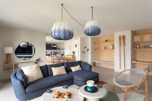 A modern living room with a sectional sofa, a coffee table with pastries, and a dining area in the background. - L'Écrin du Homard Bleu - Plein centre de Dinard (Dinard)
