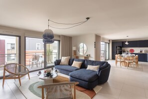 A modern living room with a sofa, chairs, a coffee table, and a dining area with a kitchen in the background. - L'Écrin du Homard Bleu - Plein centre de Dinard (Dinard)