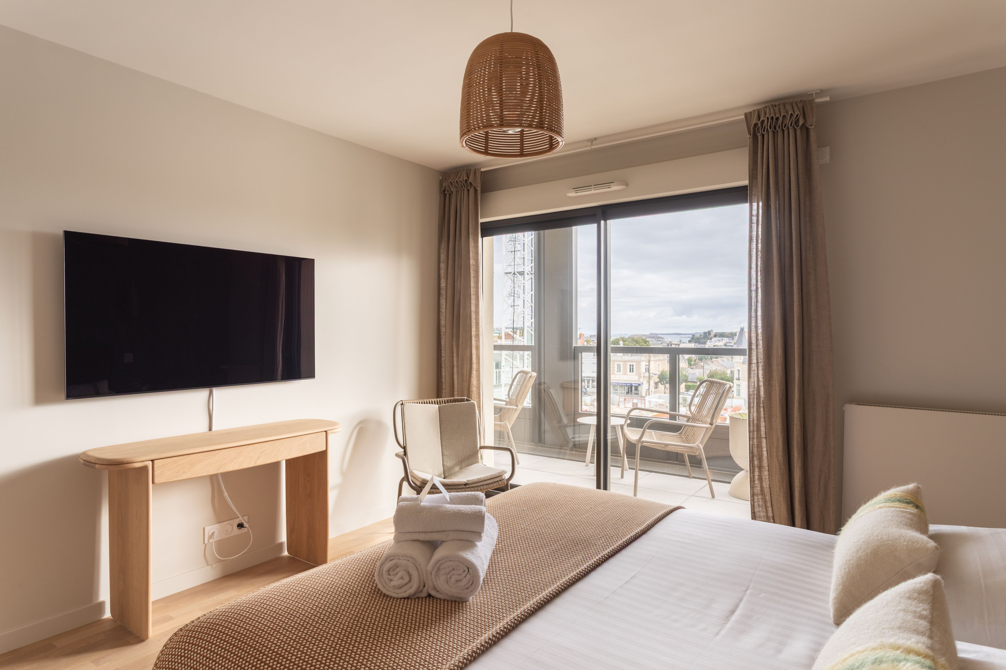 A hotel room with a bed, a TV, a desk, a chair, and a balcony with a view.