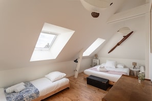 Quarto com teto inclinado, duas camas, uma mesa de madeira e um ventilador de teto.