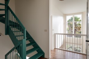 Uma escadaria com corrimãos verde-água que leva a uma varanda com corrimão branco.