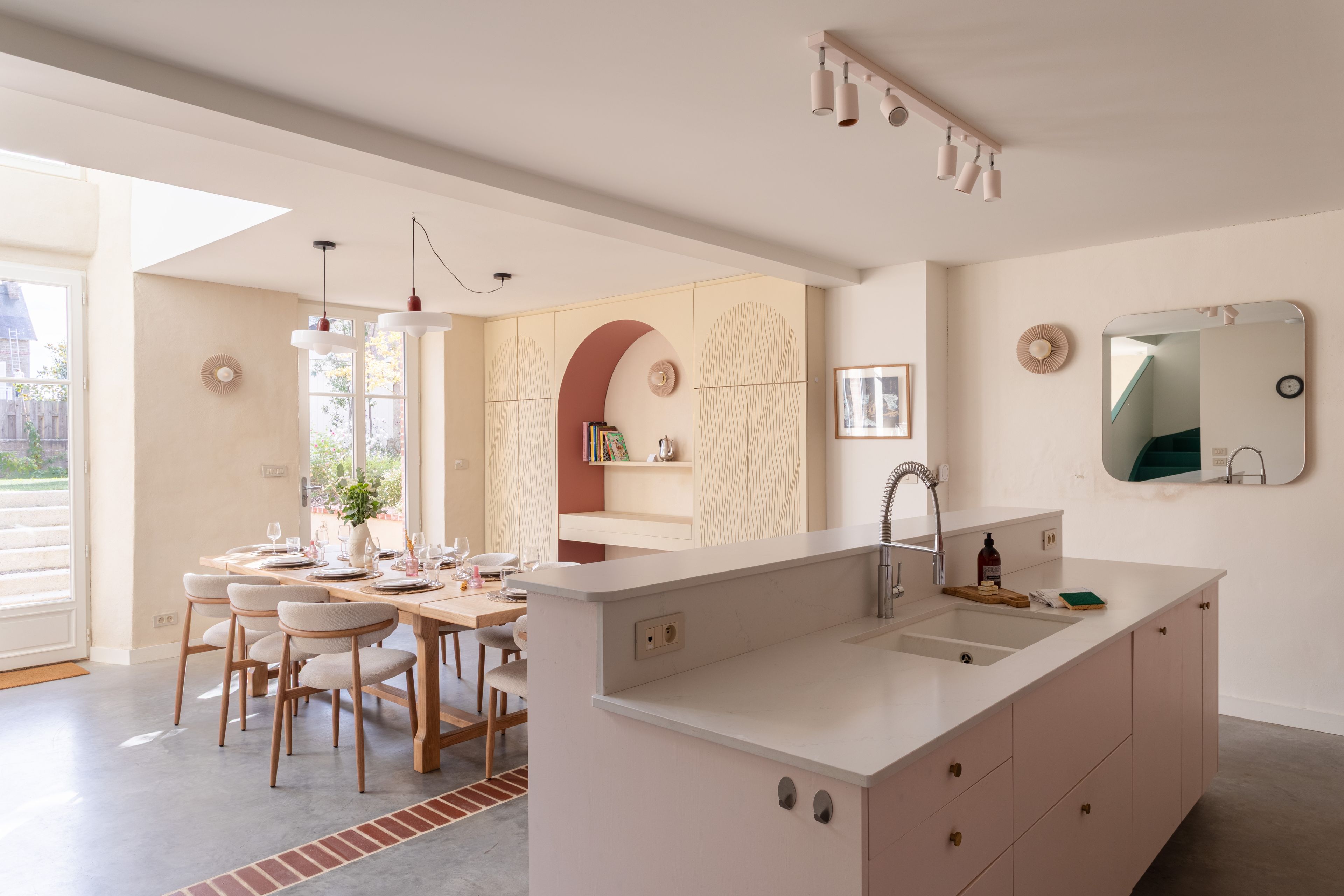 Cuina moderna amb una illa central, zona de menjador amb cadires i una finestra gran.