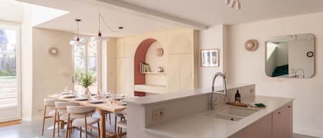 A modern kitchen with a central island, a dining area with chairs, and a large window.