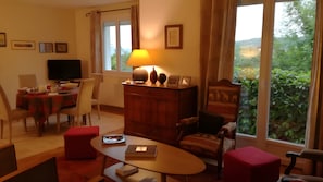 Un salon comprenant un coin repas, un téléviseur, une lampe et donnant sur un espace verdoyant.