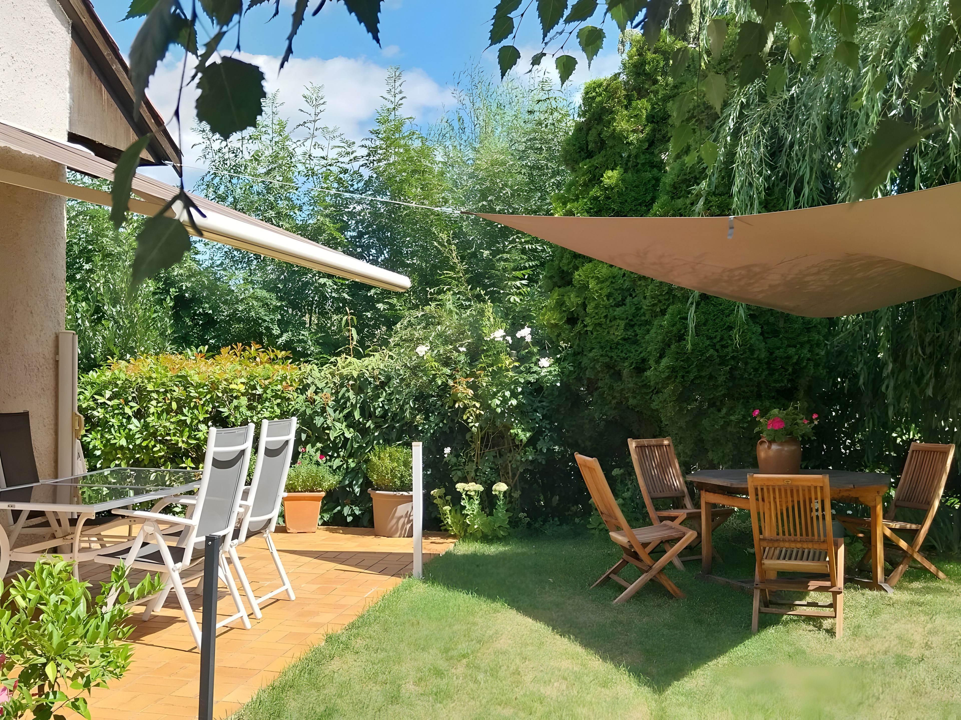An outdoor patio with a table and chairs, surrounded by greenery and a pergola.
