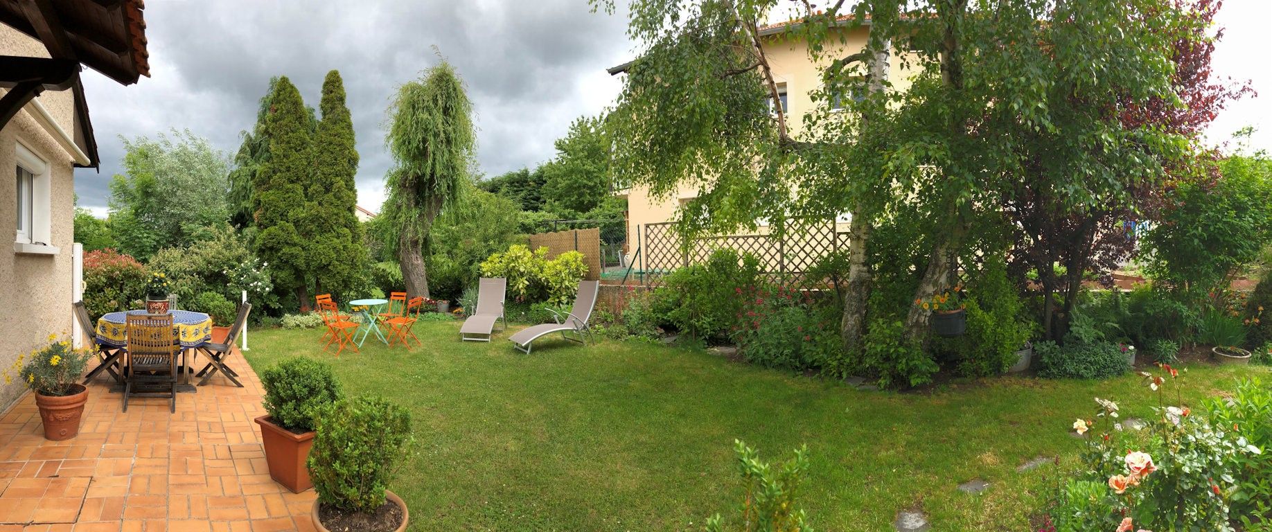 A garden with a patio area, a lawn, and various plants.