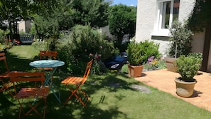 Un jardin avec une table et des chaises, des plantes en pot et une voiture garée au fond.