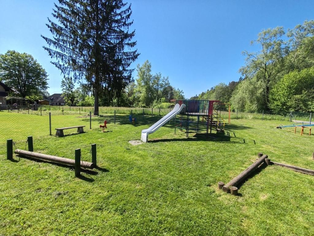 Un parque infantil con tobogán y estructuras para escalar, rodeado de césped y árboles.