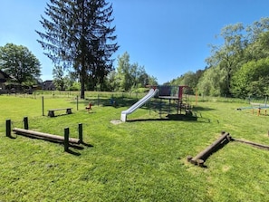 Un parque infantil con tobogán y estructuras para escalar, rodeado de césped y árboles.