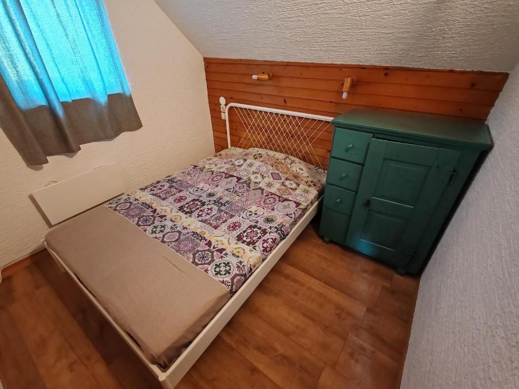 A small room with a single bed, a wooden headboard, a green dresser, and a window with curtains.