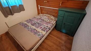 A small room with a single bed, a wooden headboard, a green dresser, and a window with curtains.