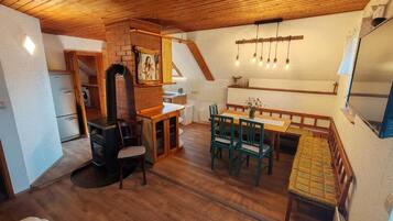 A cozy room with a wooden ceiling, a dining table with chairs, a fireplace, and a bed.