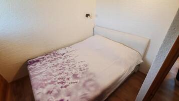 Ein kleines Zimmer mit einem Einzelbett, einem schlichten weißen Kopfteil und einer zudeckenden Bettdecke mit Blumenmuster.