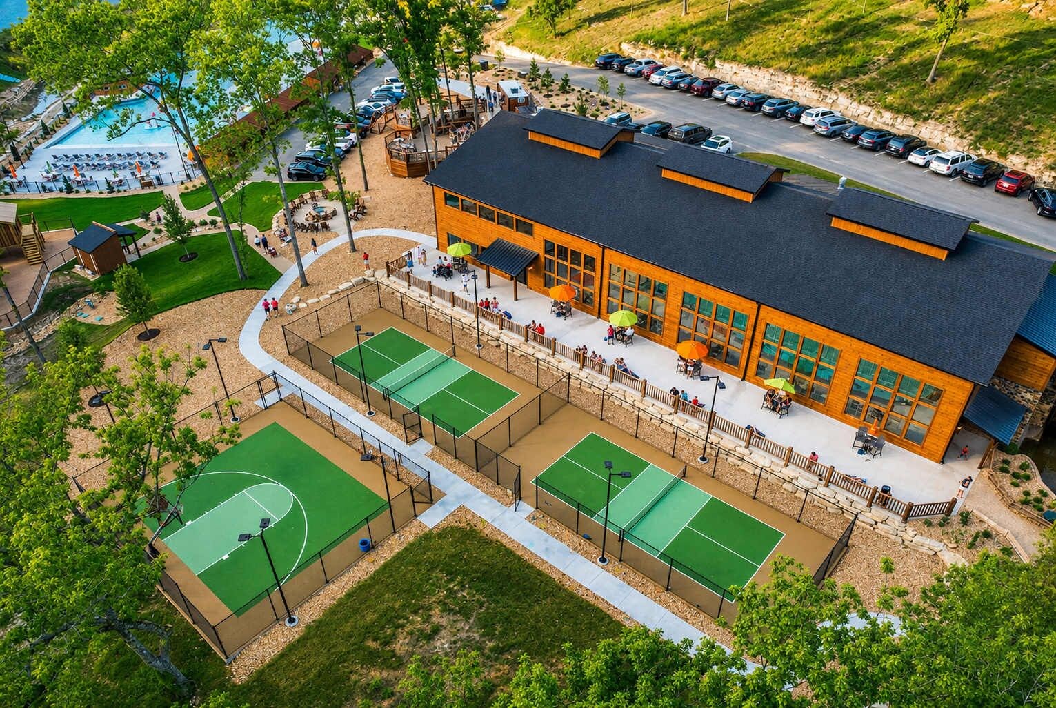 Een meerhoog gebouw met een tennisbaan, terras en parkeerplaats.