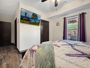 Een slaapkamer met een bed, een deur, een raam met gordijnen en een muur met een schilderij.