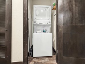 Ein Waschraum mit einer Waschmaschine und einem Trockner, Holztüren und einer kleinen Ablage für Reinigungsmittel.