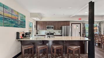 Une cuisine moderne avec un îlot central, des tabourets de bar, des appareils en acier inoxydable et un tableau accroché au mur.