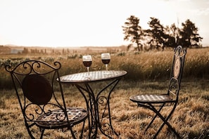 A metal table and two chairs in a grassy field with two glasses of wine.