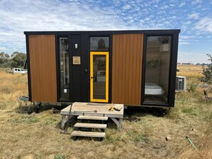 Une petite cabane avec une façade en bois, une porte jaune et un banc à l’extérieur.