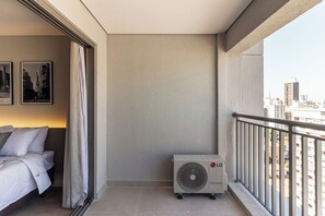 Quarto de hotel com cama, janela com cortinas, ar-condicionado fixado na parede e vista para a cidade.