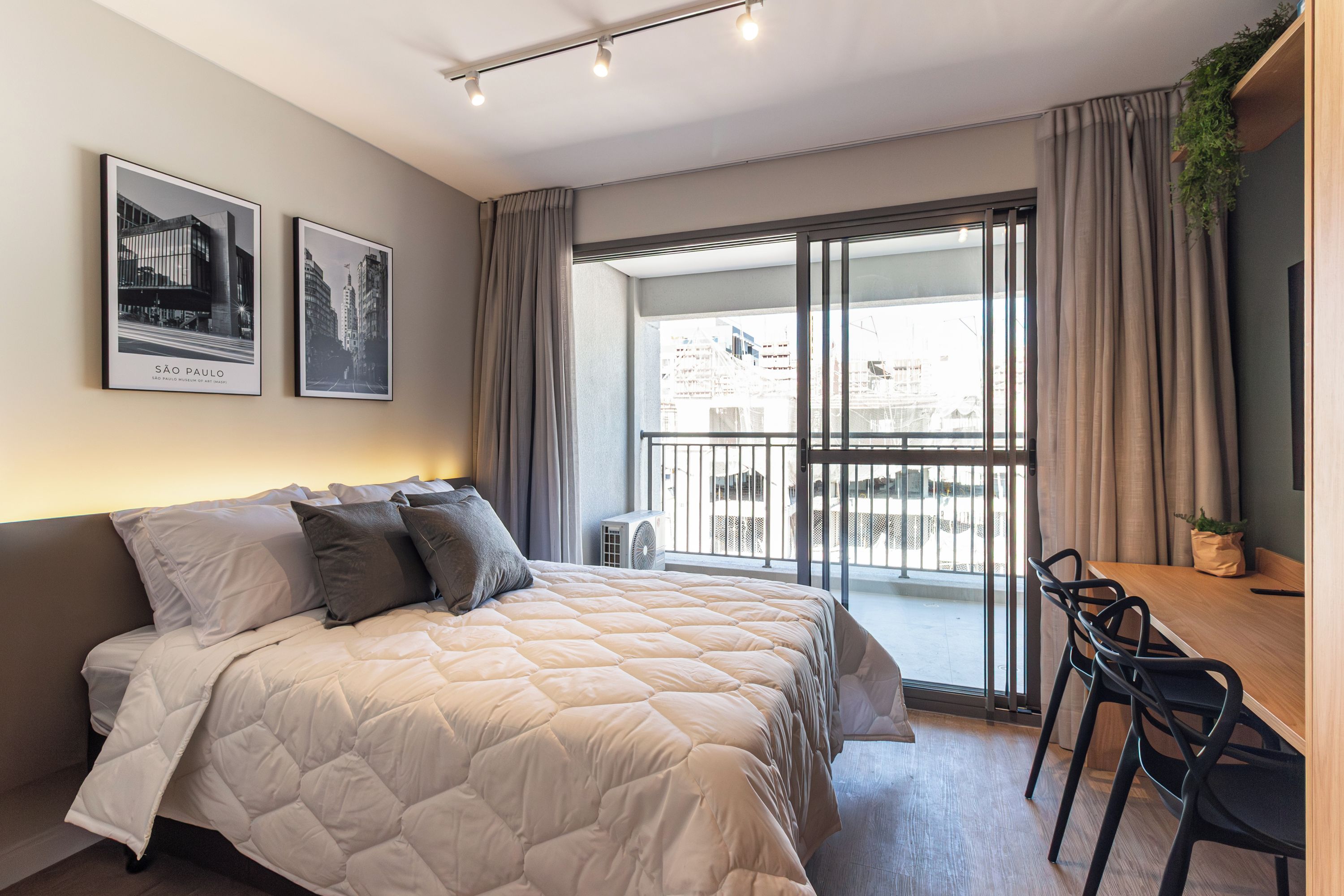 Quarto moderno com cama grande, escrivaninha com cadeiras e varanda com vista.