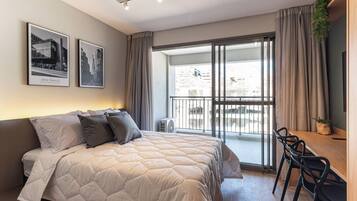 Quarto moderno com cama grande, escrivaninha com cadeiras e varanda com vista.