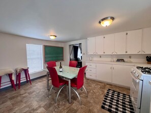 Una cocina compacta con armarios blancos, estufa a gas y comedor con mesa y sillas rojas.