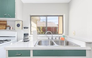 A kitchen with a double sink, a blender, a gas stove, and a window with a view of a building outside.