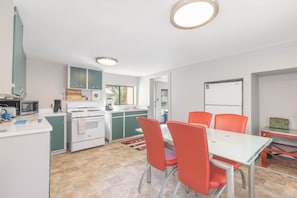 A modern kitchen with white appliances, green cabinets, and a dining area with red chairs.
