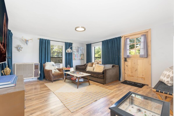 A furnished living room with a sofa, armchair, coffee table, and a door with a window.