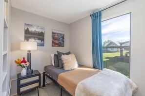 A bedroom with a bed, a nightstand, a lamp, a vase with flowers, and two wall-mounted pictures.