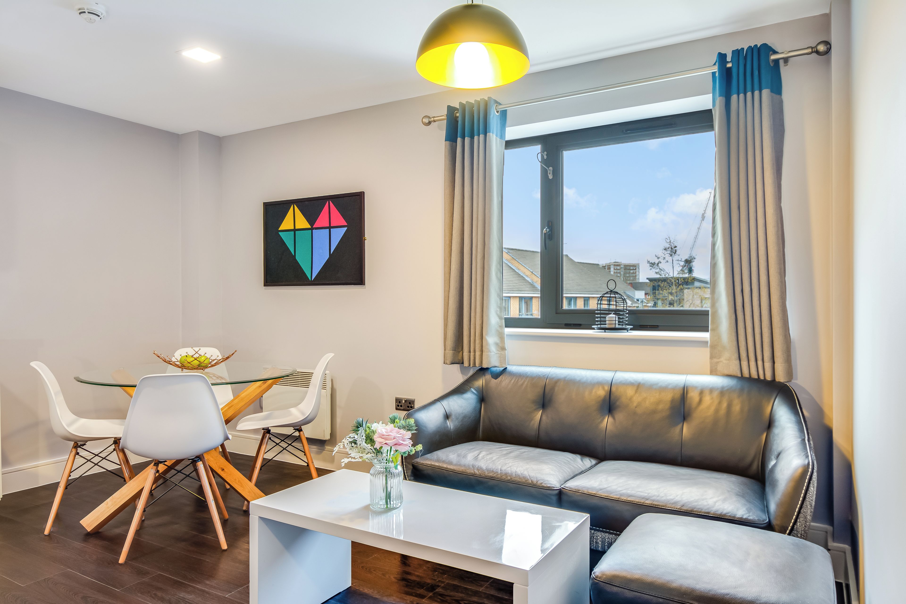 A modern living room with a leather sofa, a glass coffee table, and a dining area with a white table and chairs.