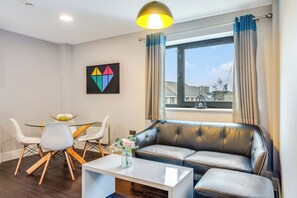 Uma sala de estar moderna com um sofá de couro, uma mesa de centro de vidro e uma área de jantar com mesa e cadeiras brancas.